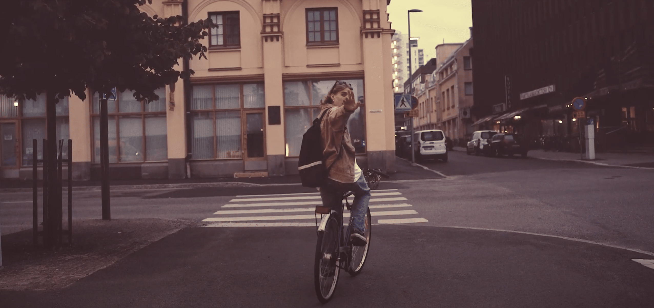A person riding a bicycle through a city street and waving at the camera.