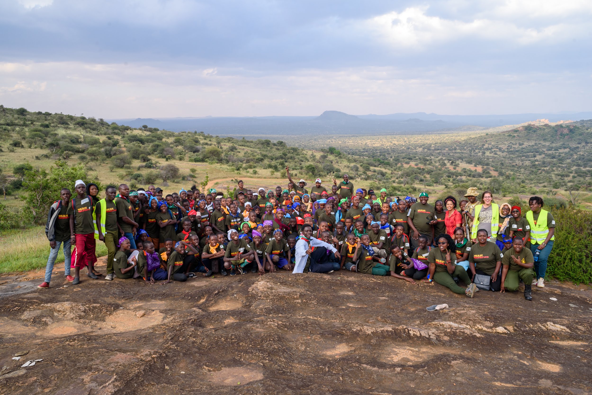 A large group of people posing in front of a Kenyan scrubland landscape.
