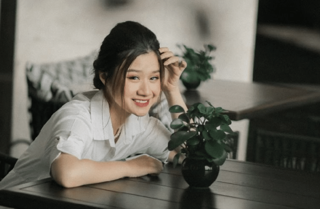 Minh Anh Le sits at a table and smiles with a plant